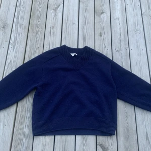 Mörkblå stickad tröja från COS - Snygg mörkblå stickad tröja från COS i storlek XS. Tröjan har v-ringad hals och är gjord i ull. Då tröjan har textilfibrer så säljs tröjan extra billigt. 