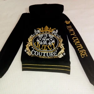 Juicy Couture velourjacka - Svart velourjacka från Juicy Couture med guld- och silver tryck på ryggen och ärmen. Jackan har huva, dragkedja och två fickor fram. Snygga guldränder vid midjan och ärmsluten ger extra bling. Perfekt för dig som vill sticka ut med en ikonisk streetstil. Jackan är använd men i bra skick och har inga hål eller fläckar.det är storlek S men är liten i strl och sitter som en XS.