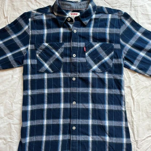 Levi’s Herrskjorta i Flanell, Blå/Rutigt – Storlek M - Skön skjorta i mjuk flanell från Levi’s, perfekt för vardag och casual stil. Fint begagnat skick med bevarad färg och hela knappar. Tidlös modell med två bröstfickor och knäppning hela vägen fram. 	•	Märke: Levi’s 	•	Storlek: M (herr) 	•	Färg: Blå med rutmönster 	•	Material: Mjuk flanell 	•	Passform: Normal 	•	Skick: Fint begagnat, inga fläckar eller skador Mått: 	•	Bröst: 43 cm 	•	Längd: 67 cm 	•	Ärmlängd: 55 cm. Snabb leverans!