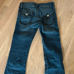 Mörkblå jeans  - Snygga mörkblå jeans och klassisk femficksdesign. Jeansen har slitningar och kontrastsömmar, samt bakfickor med lock och knapp. Perfekta för en avslappnad och cool stil.