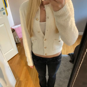 Vit kofta med guldknappar - Superfin vit/ljusbeige croppad kofta med guldiga knappar och två små fickor framtill. Mjuk och fluffig känsla, perfekt till jeans eller kjol. Långärmad och med en snygg v-ringning som ger en trendig look. Använd fåtal gånger. 🩷