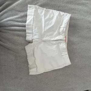 Vita shorts från H&M med fickor - Snygga lågmidjade vita shorts från H&M med klassisk design och raka ben. Shortsen har två fickor bak och hällor för bälte. Perfekta för varma dagar och enkla att matcha med allt. Tillverkade i bomull för en skön känsla.