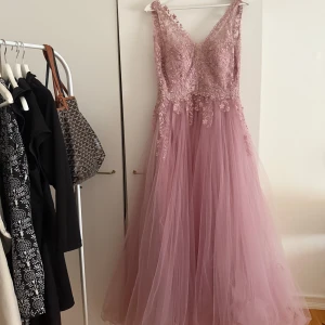 Rosa balklänning/gamlas dans från Linda Pereira -  rosa balklänning från Linda Pereira med v-ringad spetsliv och voluminös tyllkjol. Klänningen har  spetsdetaljer upptill och är ärmlös, perfekt för bal eller gamlas dans.