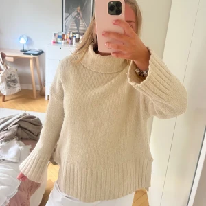Beige stickad polotröja i oversized modell - Supermysig beige stickad polotröja med breda ribbade muddar och hög krage. Tröjan har en loose och oversized passform, perfekt för lager på lager. Passar dig som gillar en chill och avslappnad stil under kyliga dagar.