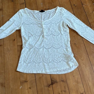Vit spetsblus med knappar - Säljer en vit blus med spetsmönster och rundad hals. Blisen har små knappar framtill. Den är lätt transparent och har en feminin, smickrande passform. 
