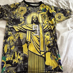 Brasilien Ronaldo fotbollströja - Unik Brasilien fotbollströja med Ronaldo #9, coolt grafiskt tryck med Kristusstatyn och brasilianska motiv i svart och gul. Kortärmad modell med broderat CBF-märke och detaljer i grönt. Tillverkad i lätt polyester, perfekt för dig som vill sticka ut på läktaren.