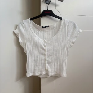 Vit croppad ribbad topp med knappar - Supersöt vit croppad topp från Brandy Melville med ribbad struktur och korta ärmar. Rundad halsringning och knappar framtill ger en chill vibe