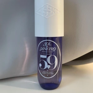 Sol de Janeiro Cheirosa 59 Perfume Mist - Fräsch och trendig body mist från Sol de Janeiro i doften Cheirosa 59. Flaskan är lila med vit spraypump och lock. Perfekt att ha med i väskan för en snabb uppfräschning. Snygg design med tydlig logga och siffran 59 på framsidan.