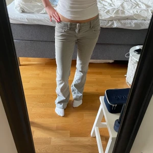 Lågmidjade ljusgrå bootcut jeans - Säljer ett par grå jeans med låg midja och bootcut-ben. Jeansen har klassisk femficksdesign, bälteshällor och stängs med knapp och dragkedja. Midjemått 37 och innebenslängd längd 77, jätte stretchiga i materialet i midjan och låren 