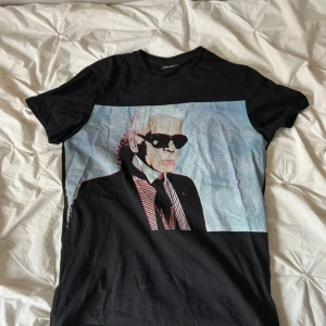 Svart t-shirt med tryck Karl Lagerfeld - Svart t-shirt från Karl Lagerfeld i storlek M med coolt grafiskt tryck på framsidan. Materialet är mjuk bomull och passformen är normal. 🥰