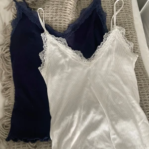 Två ribbade linnetoppar med spets - Säljer två ribbade linnetoppar från AMISU, en vit med vit spetskant och en mörkblå med blå spetskant. Säljer även dessa separata för 39kr/st.