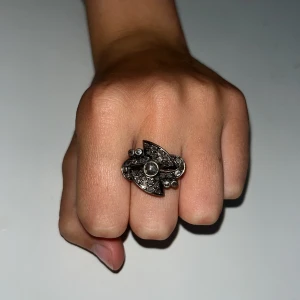 Unik silverring med glittriga stenar - Säljer en cool och annorlunda silverring med glittriga stenar i ett futuristiskt mönster. Ringen har en stor rund sten i mitten och flera mindre stenar runtom, vilket ger den extra bling. Perfekt för dig som vill sticka ut med din stil!