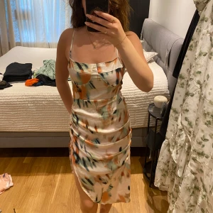 Mönstrad satin klänning med slits - Säljer en kort klänning i satin med smala axelband, figurnära passform och snygg slits på sidan. 