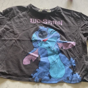 Svart Lilo & Stitch t-shirt från H&M - Cool svart t-shirt från H&M med stort Lilo & Stitch-tryck framtill. T-shirten har korta ärmar, rund hals och är gjord i mjuk bomull. Perfekt för dig som älskar Disney och vill ha en avslappnad och lekfull stil. 20 kr +frakt, 134/140 storlek