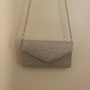 Glittrig silver kuvertväska med kedja - En så söt kuvertväska med kedja ifrån Glitter! Väskan har en avtagbar kedja. PS. Väskan är väldigt liten (endast ca 18cm bred). Säljs för 40kr!!💕