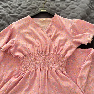 Rosa blommig långklänning från S.L.C.E - Supersöt rosa långklänning med små blommor i gult och blått. Klänningen har omlott-v-ringning, korta ärmar och smockad midja som ger en snygg siluett. Perfekt för sommarens alla tillfällen! Materialet känns lätt och luftigt. Mycket bra skick. Storleken är ganska liten då den passar mig som har storlek S/XS. 