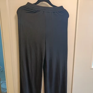 Svarta ribbade byxor med resår - Säljer ett par svarta byxor med ribbad struktur och bekväm resår i midjan. Byxorna har en rak och loose passform, perfekta för en chill och avslappnad stil. Materialet känns mjukt och följsamt mot huden.