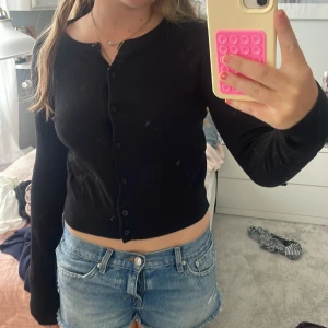 Svart kofta från H&M, storlek S - Svart, croppad kofta från H&M i storlek S. Koftan har rund hals, långa ärmar och knappar hela vägen framtill. Materialet är mjukt och lätt, perfekt att slänga över en topp. Enkel och stilren design som funkar till jeans eller kjol.