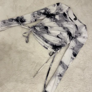 Svartvit långärmad topp med snörning - Säljer en svartvit långärmad topp med coolt mönster och snörning i sidorna. Toppen har en tight passform och är perfekt för dig som gillar unika detaljer och trendig stil.