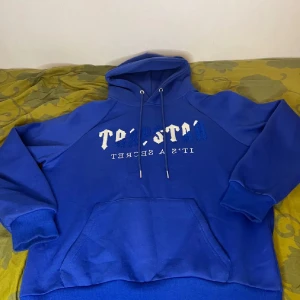 Blå hoodie med tryck och huva - Snygg blå hoodie med vit och blå text framtill och stor magficka. Tröjan har huva med snörning och långa ärmar med muddar. Perfekt för dig som gillar streetstyle och vill ha en bekväm och cool look.