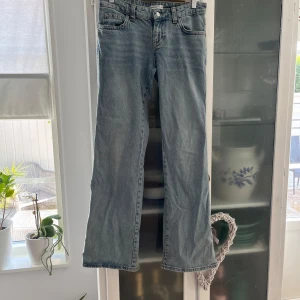 Ljusblå low boot-cut jeans från Gina TRICOT  - Snygga ljusblå jeans från Gina Tricot i boot-cut modell low waist med klassiska fem fickor och coola ficklock bak. Jeansen har normal passform och är tillverkade i slitstarkt denim. Perfekta för dig som gillar en avslappnad och trendig look. Använda 2 gånger.