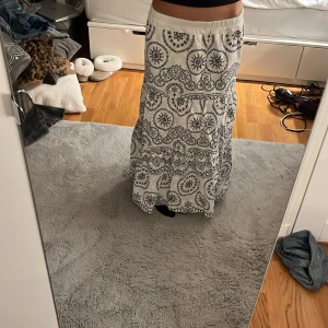 Vit långkjol med svart mönster - Säljer en vit långkjol med blå, detaljerat mönster. Kjolen har en elastisk midja. Andvönd Max 5-6 gånger.