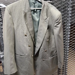 Beige dubbelknäppt kavaj - Stilren beige dubbelknäppt kavaj med diskreta ränder och klassiska slag. Kavajen har fyra knappar framtill, två fickor med lock och en bröstficka. Perfekt för dig som gillar en tidlös och elegant look.