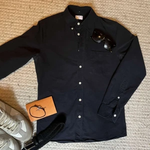 Mörkblå skjorta från ASKET i bomull - Klassisk mörkblå skjorta från ASKET med button-down krage och vita knappar. Skjortan har en bröstficka och är tillverkad i mjuk bomull. Perfekt för en clean och stilren look. Nypris ligger på 1800kr. Skjortan är i nyskick och i storleken XS - Regular. Inga defekter eller skavanker. 