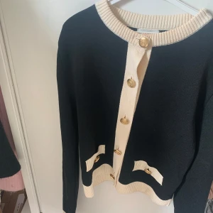 Svart och beige kofta från H&M - Snygg svart beige kofta med fina guld knappar. Den är använd fåtal gånger men den har inga tecken på användning.