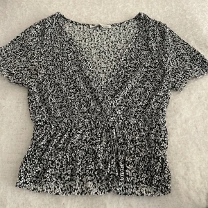 Svartvit blommig omlottblus -  svartvit blommig blus med v-ringnin och liten knytning framtill. 