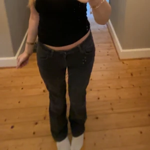 Mörkgrå bootcut jeans med låg midja - Säljer ett par mörkgrå jeans med bootcut-modell och låg midja. Jeansen har klassiska fem fickor, bälteshällor och är tillverkade i ett mjukt denimtyg. Snygg tvättad finish och passar perfekt till sneakers eller boots.