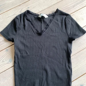 Svart ribbad topp med spets från H&M - Använt fåtal gånger men otroligt snygg om du stylar med ett par smycken o lågmidjade jeans!💗Tröjan är från H&M och har lite spets!