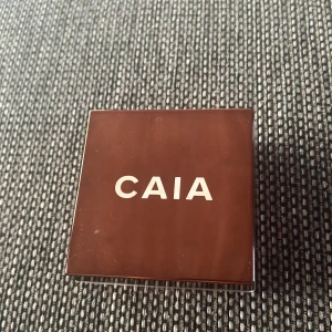 CAIA Loose Glow Bronzer Florence - Säljer en CAIA Loose Glow Bronzer i nyansen Florence. Det är ett löspuder med skimrande finish som ger en solkysst look. Kommer i en fyrkantig, transparent plastburk med sifterlock för enkel applicering. Perfekt för att highlighta och ge glow till ansiktet.