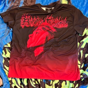 Billie Eilish x Bershka svart/röd t-shirt - Cool t-shirt från Billie Eilish x Bershka i svart och rött med stor grafisk print av Billie Eilishs ansikte och eldigt röd text. T-shirten har rund hals och korta ärmar, tillverkad i mjuk polyester. Perfekt för dig som vill sticka ut med din stil.