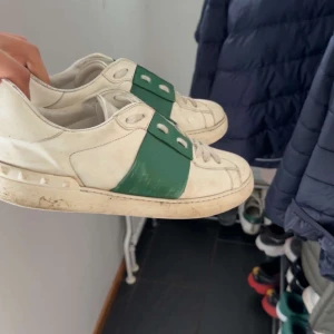 Valentino Garavani Open sneakers vit/grön - Säljer ett par Valentino Garavani Open sneakers i vitt skinn med bred grön läderdetalj över snörningen.  Snygg och stilren design som sticker ut med den gröna panelen. Sälj för jag inte använder dem längre. Hör av dig om du har frågor eller funderingar!😊
