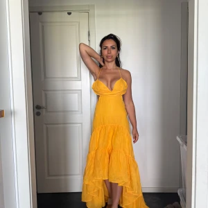 Gul långklänning med volanger - Säljer en superfin gul långklänning med volanger och djup v-ringning. Klänningen har halterneck och öppen rygg, vilket ger en riktigt somrig vibe. Perfekt för dig som vill sticka ut med en färgglad och flowy look!