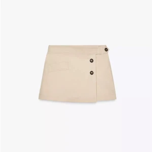 Beige kortkjol med knappar - Snygg beige kortkjol med omlott-design och svarta knappar framtill. Kjolen har en fickdetalj på sidan.