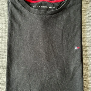 Tommy Hilfiger T-shirt  - Klassisk svart T-shirt från Tommy Hilfiger, en diskret, broderad logga på bröstet. En tidlös baströja i mjukt material som passar perfekt till både vardags och mer uppklädda outfits. Bra skick och redo att bäras vidare!