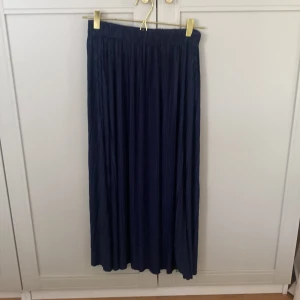 Mörkblå plisserad långkjol Samsøe Samsøe - Supersnygg mörkblå plisserad långkjol från Samsøe Samsøe. Kjolen har ett elastiskt midjeband och faller riktigt fint med sina tunna veck. Perfekt för dig som gillar stilrena och klassiska plagg med lite extra flow.
