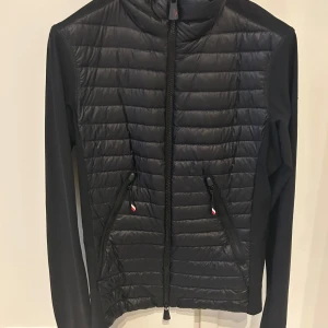 Svart Moncler Grenoble pufferjacka - Snygg svart jacka från Moncler Grenoble med quiltad framsida och släta ärmar och rygg. Jackan har dragkedja framtill, två snedställda fickor med dragkedja och diskreta logodetaljer. Jackan är storlek xs men skulle mer säga att den passar s-m. Finns tyvärr 3 små hål på ryggen men inget man tänker på så Nypris är 8000kr, kvitto finns kvar