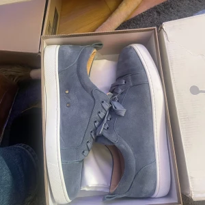 Christian Louboutin  - Snygga sneakers i blå mocka med klassisk design och vit platt sula. Skorna har rund tå, snörning och diskreta detaljer.
