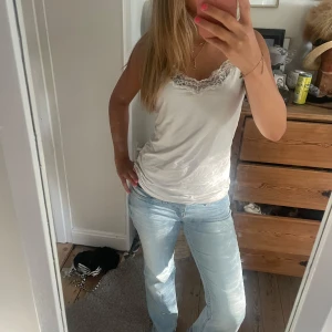 Vit linnetopp med spetsdetalj - Säljer en söt vit linnetopp med tunna axelband och spetskant vid urringningen. Toppen är figurnära och har en enkel, stilren look som passar till både som ett linne eller under en kofta 