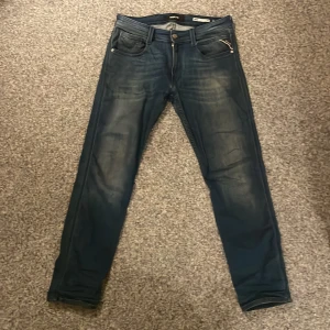 Replay Anbass slim fit jeans blå (pris kan diskuteras) - Snygga blå Replay Anbass jeans i slim fit med klassisk femficksdesign och coola slitningar. Jeansen har en mörk tvätt och detaljer som dragkedja och Replay-lapp bak i midjan. Perfekta för dig som gillar en smalare passform och stilren look.