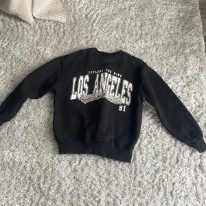 Svart sweatshirt från Pull&Bear - Säljer en svart sweatshirt från Pull&Bear med texten 'Los Angeles' i vitt och grått på framsidan. Tröjan har långa ärmar och en rund halsringning. Perfekt för en avslappnad stil. 🖤 superskön, endast använd ett fåtal gånger. Mitt pris 100 kr nypris 500kr