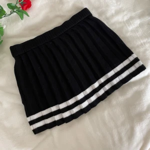 Svart kortkjol från Cherry Mellow - Snygg svart kortkjol från Cherry Mellow med vita ränder längst ner. Kjolen har en ribbad struktur och en elastisk midja för bekväm passform. Perfekt för en trendig look! Ny utan prislapp. Mått - midja: 36cm - Längd: 34cm