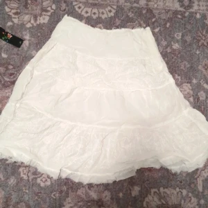 Vit kjol från ONLY - Säljer en söt vit kjol från ONLY med volangdetaljer. Perfekt för varma dagar och ger en romantisk touch till din outfit. Kjolen har en luftig och bekväm passform.