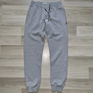 Grå mjukisbyxor från Marine Sweden - Säljer ett par grå mjukisbyxor från Marine Sweden. Byxorna har en bekväm passform med resår i midjan och snörning för justering. De har ribbade muddar vid bensluten och en knappdetalj vid fickan. Perfekta för en avslappnad stil.