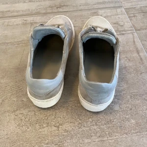 Grå sneakers med dragkedja - Snygga grå sneakers i mocka med dragkedja framtill. Perfekta för en stilren och bekväm look. De har en rund tå och en vit sula som ger en fräsch kontrast. Märket på skorna är artigato och vid snabb affär kan priset diskuteras