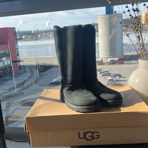 Svarta UGG Classic Tall Boots - Säljer ett par svarta UGG Classic Tall boots. De är tillverkade i mjukt skinn och har en robust sula för bra grepp. Perfekta för kalla dagar med sin varma och bekväma insida.