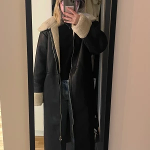 Svart lång kappa från NA-KD - En stilren svart lång kappa i läder från NA-KD med beige foder. Perfekt för kyligare dagar.